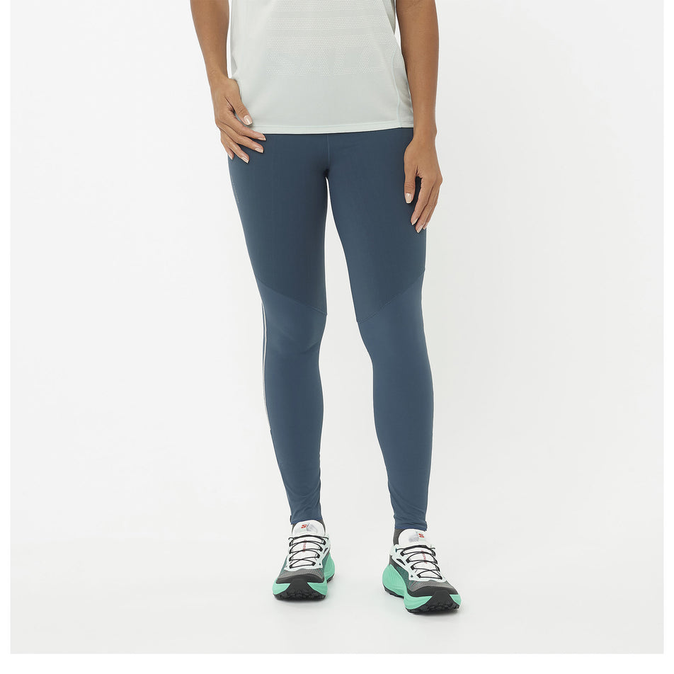 Front view of a model wearing a pair of Salomon Women's Sense Aero Stow Tights in the Midnight Navy colourway. Model is also wearing shoes and a top.  (8464096526498)