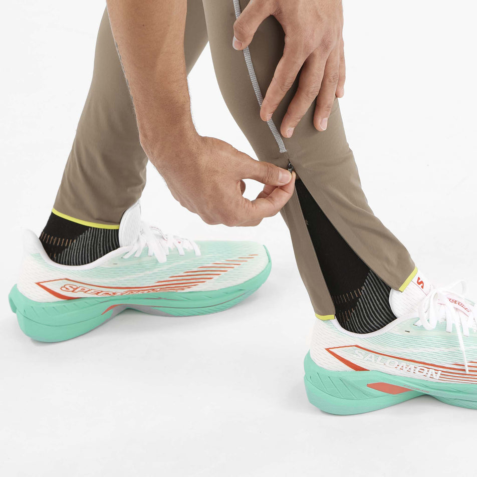 A model demonstrating the ankle zip on the lower right leg of the Salomon Men's Sense Aero Stow Tights. Tights are being worn by the model. (8509599318178)