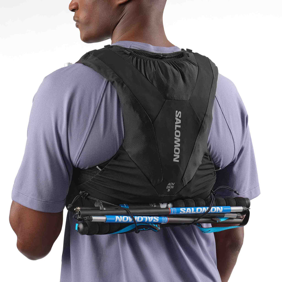 Back view of a model demonstrating the pole storage on the Salomon Unisex ADV Skin 5 Running Vest with flasks included in the Black colourway. (8575893307554)