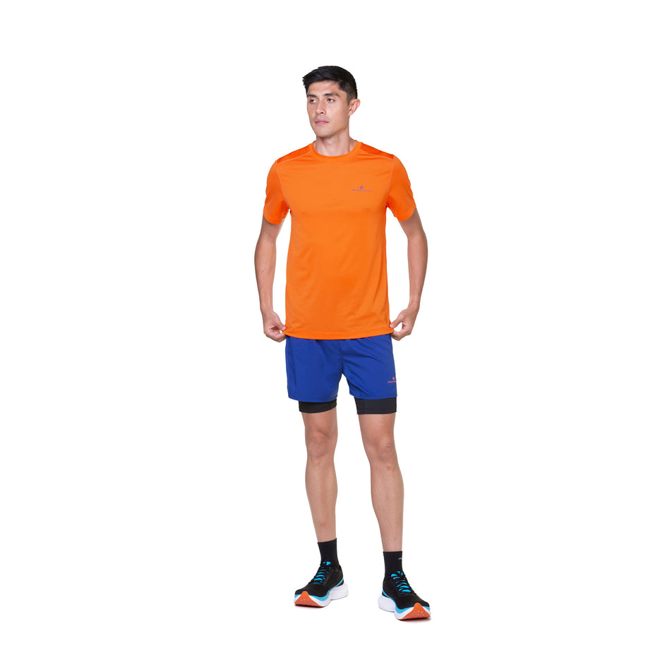 Front view of a model wearing the Ronhill Men's Tech S/S Tee in the Cardinal Orange/Orange colourway. Model is also wearing socks, shorts and shoes. (8490372726946)