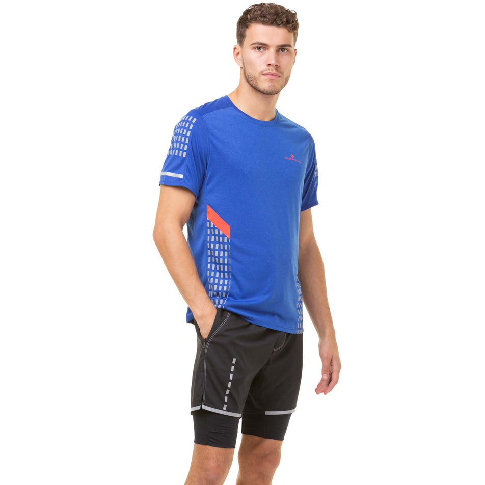 Angled front view of a model wearing a Ronhill Men's Tech Afterhours S/S Tee in the Cobalt/Flame/Reflect colourway. Model is also wearing Ronhill running shorts. (8048091725986)