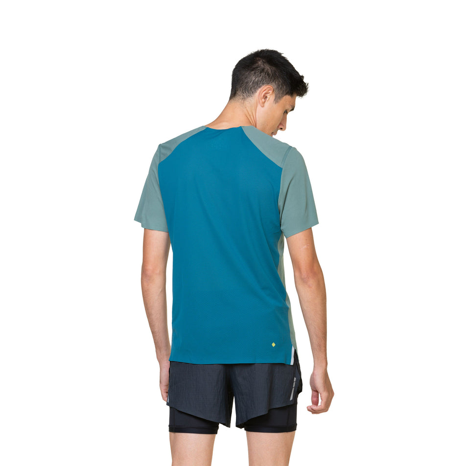 Back view of a model wearing a Ronhill Men's Tech Race S/S Tee in the Dark Sage/Deep Teal colourway. Model is also wearing shorts. (8470668345506)