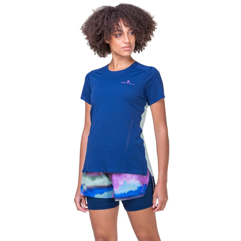 Front view of a model wearing a Ronhill Women's Tech Race S/S Tee in the Dark Navy/Honeydew colourway. Model is also wearing Ronhill shorts. (8270470578338)