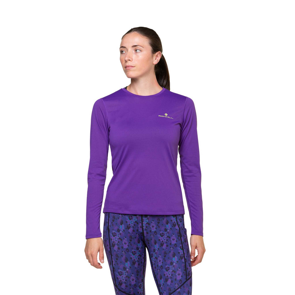 Front view of a model wearing a Ronhill Women's Core L/S Tee in the Regal Purple/Acid colourway. Model is also wearing leggings.  (8469578776738)