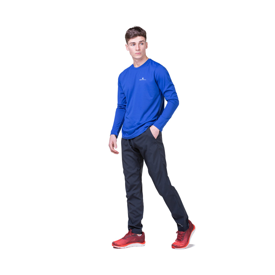 Front view of a model wearing a Ronhill Men's Core L/S Tee in the Dark Cobalt/Bright White colourway. Model is also wearing running trousers and running shoes. 
 (8468452049058)