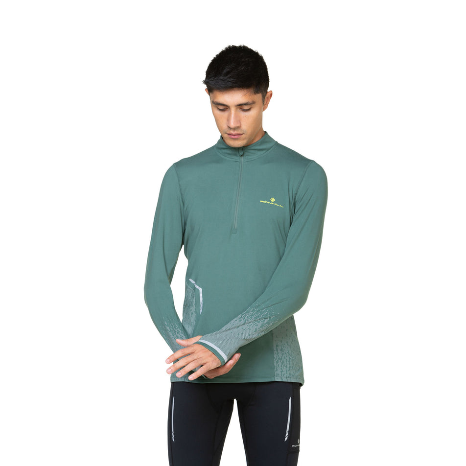 Front view of a model wearing a Ronhill Men's Tech Reflect 1/2 Zip in the Dark Sage/Reflect colourway. Model is also wearing leggings. (8490203938978)