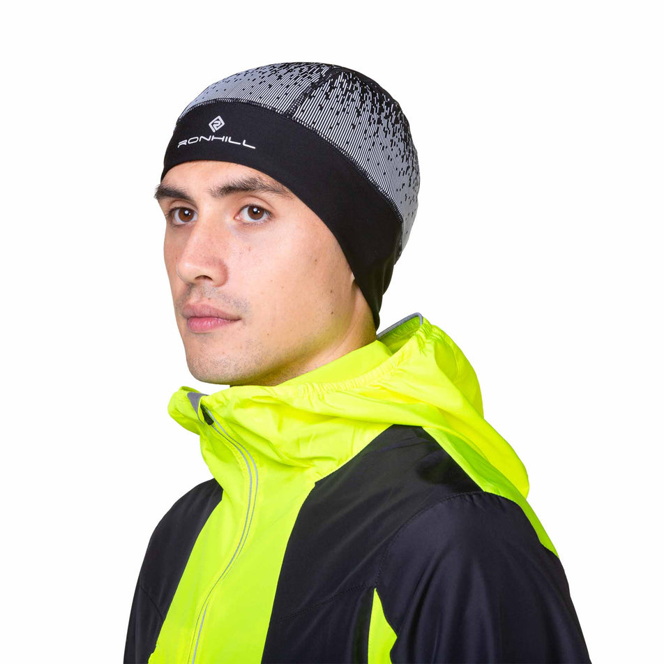 Front view of a model wearing a Ronhill Unisex Reflect Beanie in the Black/Reflect colourway. Model is also wearing a jacket. (8489141567650)