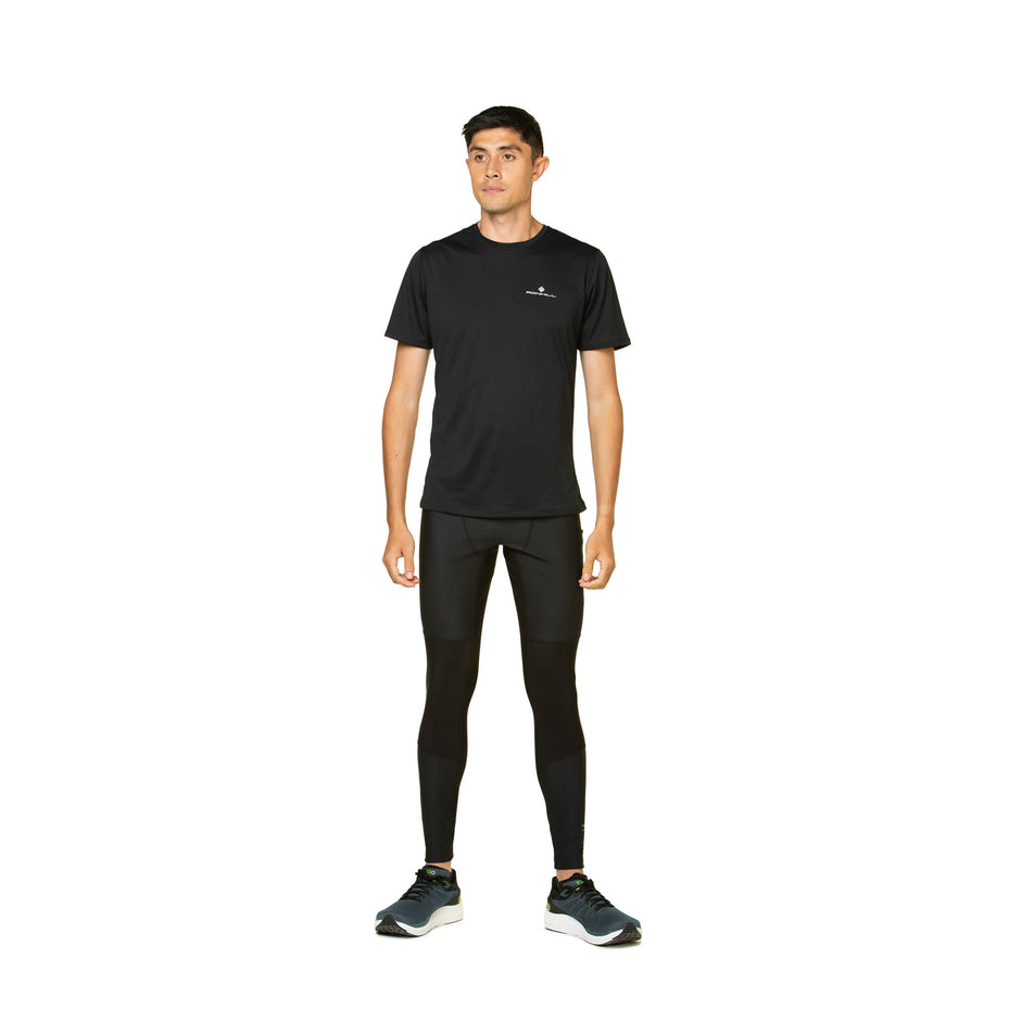 Front view of a model wearing the Ronhill Men's Tech GORE-TEX Windstopper Tight in the All Black colourway. Model is also wearing shoes and a top.  (8490245587106)