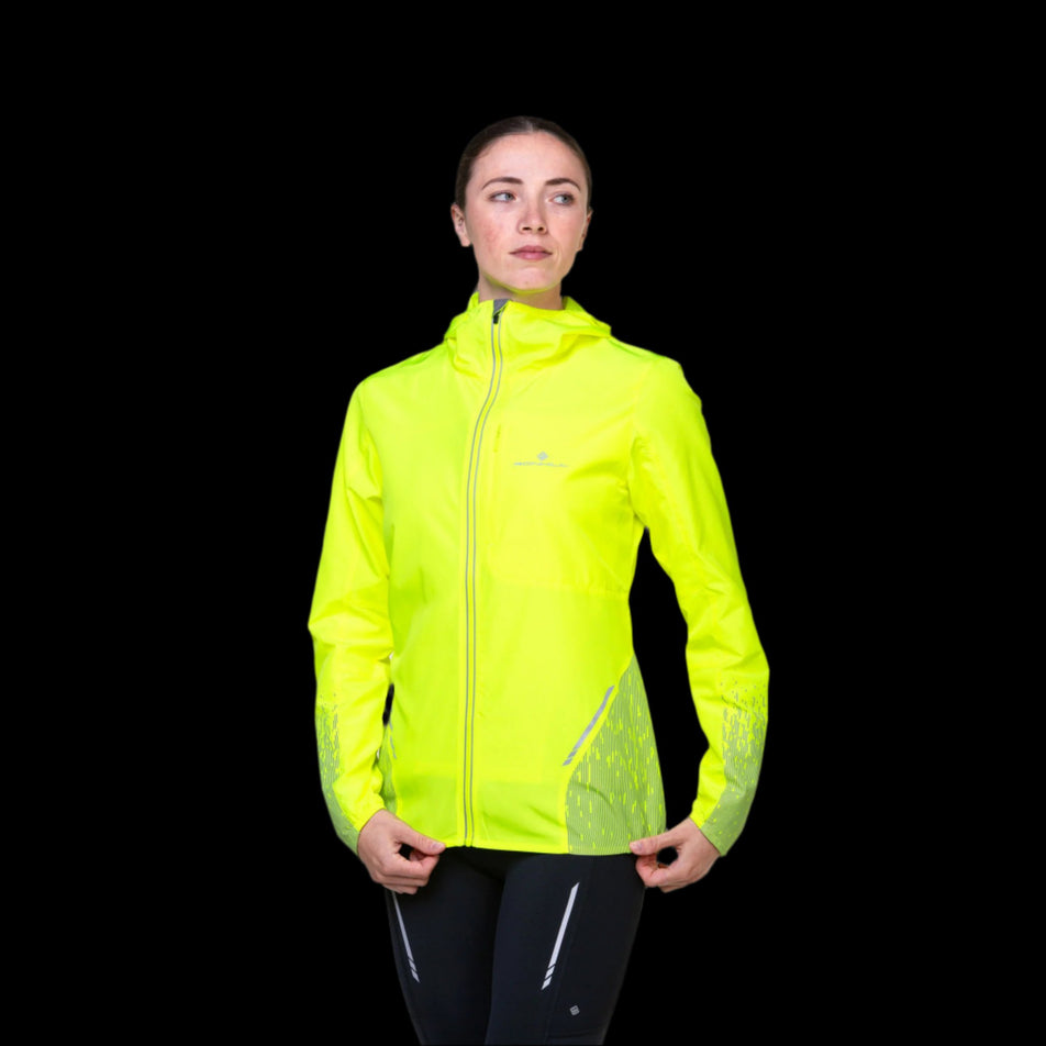 Front view of a model wearing a Ronhil Women's Tech Reflect Jacket in the Fluo Yellow/Reflect colourway. Model is also wearing leggings. (8468472463522)