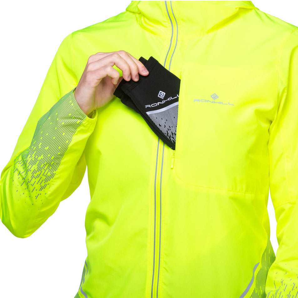 A  model demonstrating that gloves can be stored in the chest pocket of a Ronhil Women's Tech Reflect Jacket. Jacket is being worn by a model. (8468472463522)