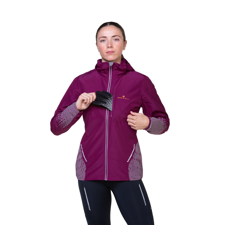 Front view of a model highlighting that gloves can be stored in the chest pocket of a Ronhill Women's Tech Reflect Jacket in the Blackcurrant/Reflect colourway. Model is also wearing tights.  (8489670607010)