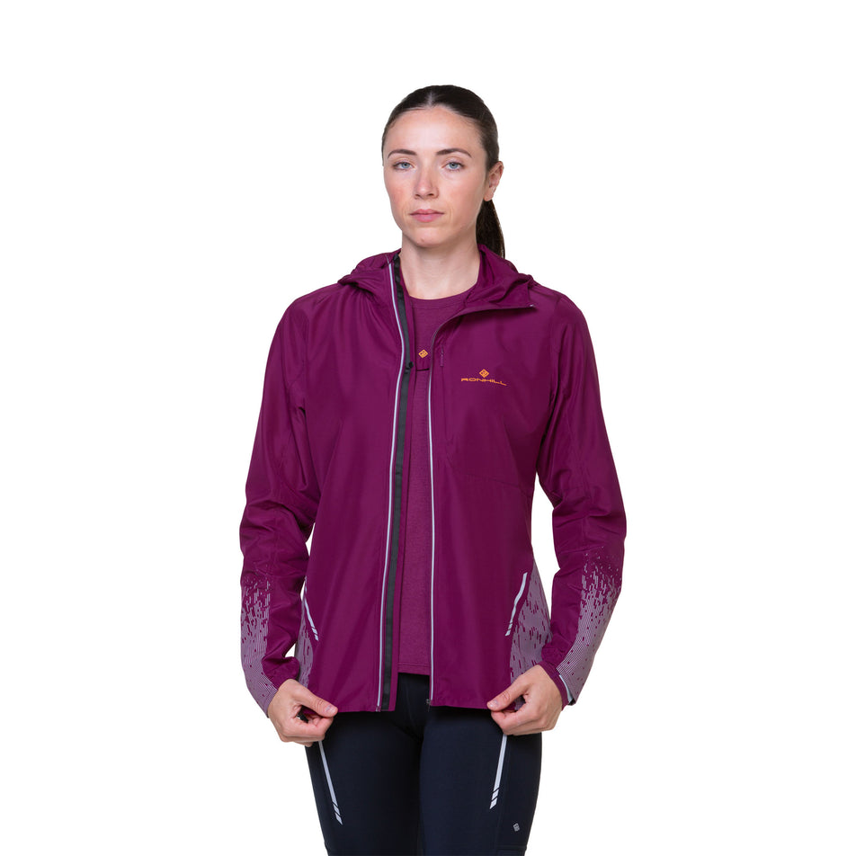 Front view of a model wearing a Ronhill Women's Tech Reflect Jacket in the Blackcurrant/Reflect colourway. Model is wearing a top underneath the jacket, and is also wearing tights. (8489670607010)