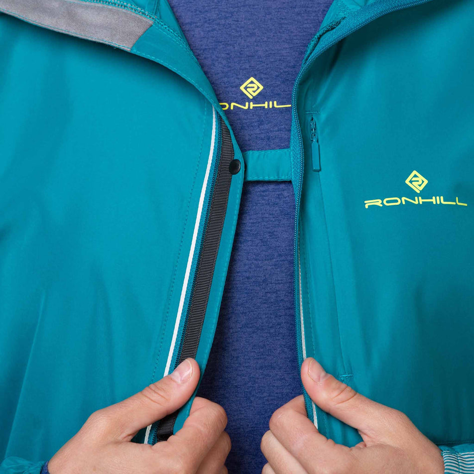 A model demonstrating the chest clip that can be used to connect the front left-side and right-side of a Ronhill Women's Tech Reflect Jacket when it is unzipped. Jacket is being worn by a model. (8469205090466)