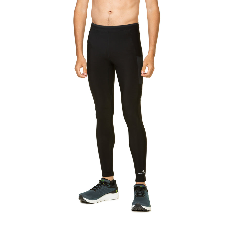 Front view of a model wearing the Ronhill Men's Tech Winter Tight in the All Black colourway. Model is also wearing shoes.  (8491238686882)