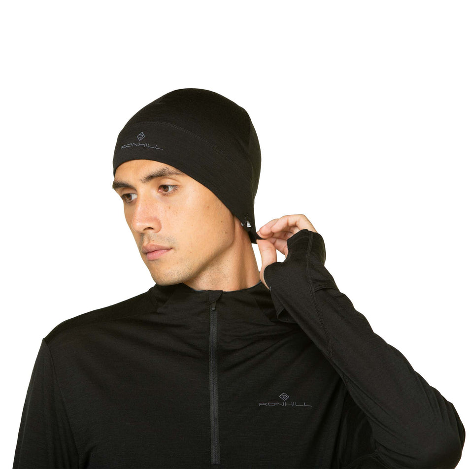 Front view of a model wearing a Ronhill Unisex Merino Beanie in the Black/Lake colourway. Model is also wearing a Ronhill top. (8489173745826)